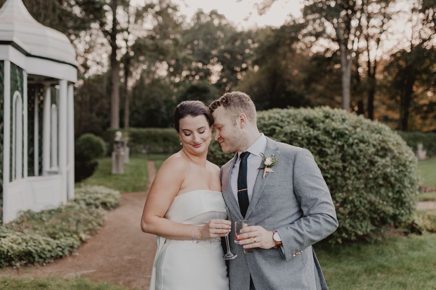 Romantic couple moment on garden path beside Victorian-style building at sunset.
