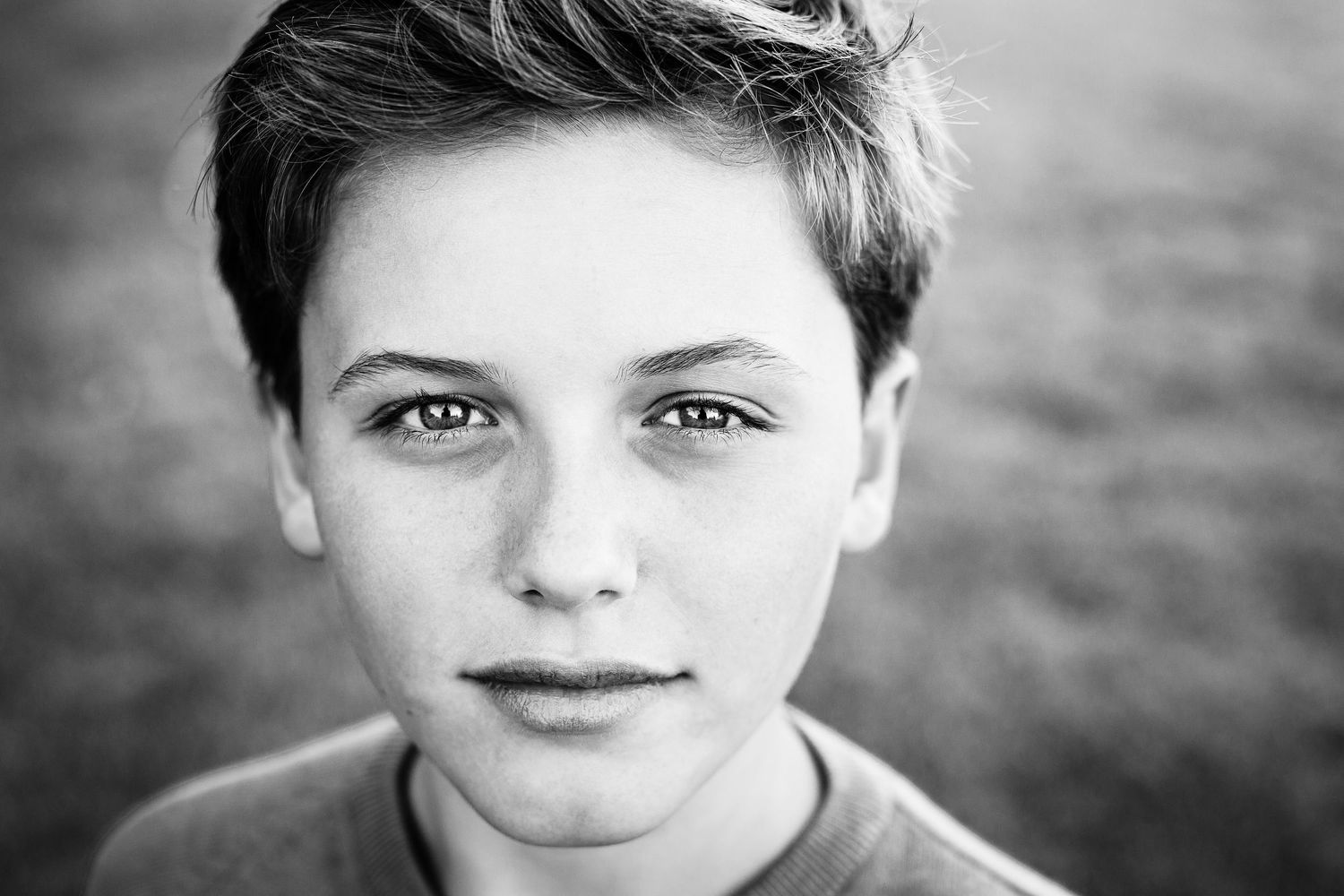 Black and white portrait of a young boy with short hair and eye-catching features in soft natural light.