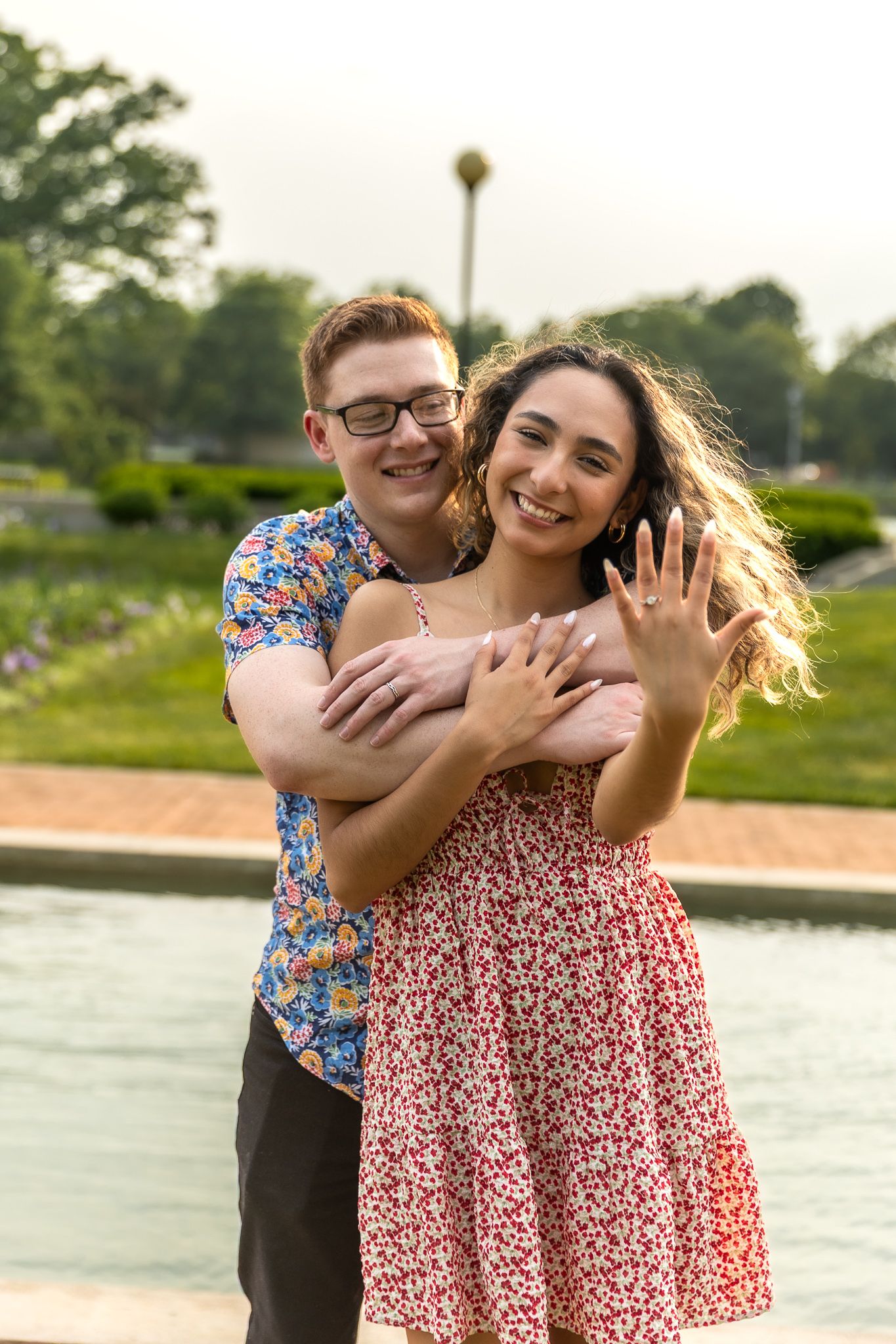 A romantic couple embraces in front of a white picket fence on a summer day.