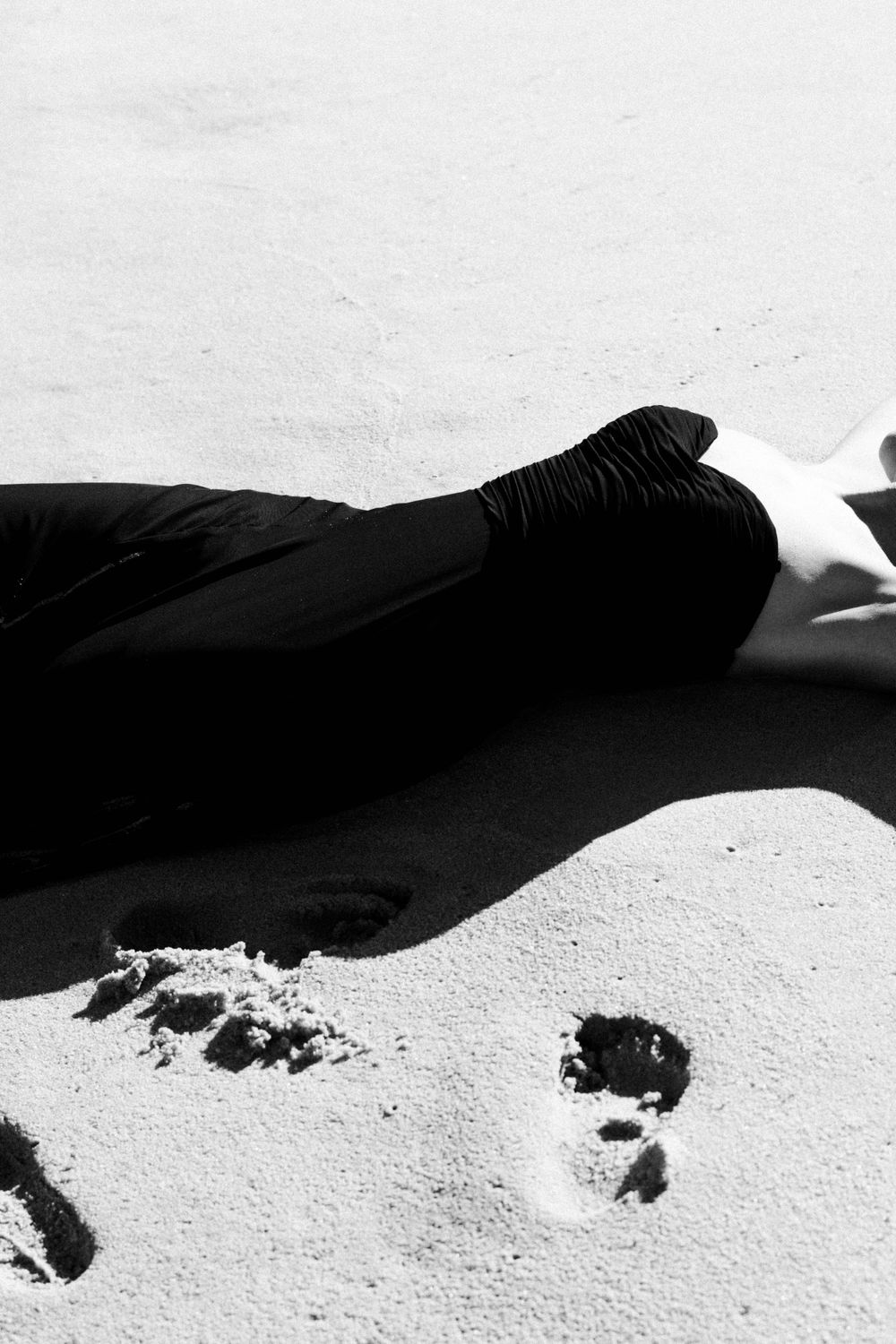 High contrast black and white photo of figure reclining on sandy surface.