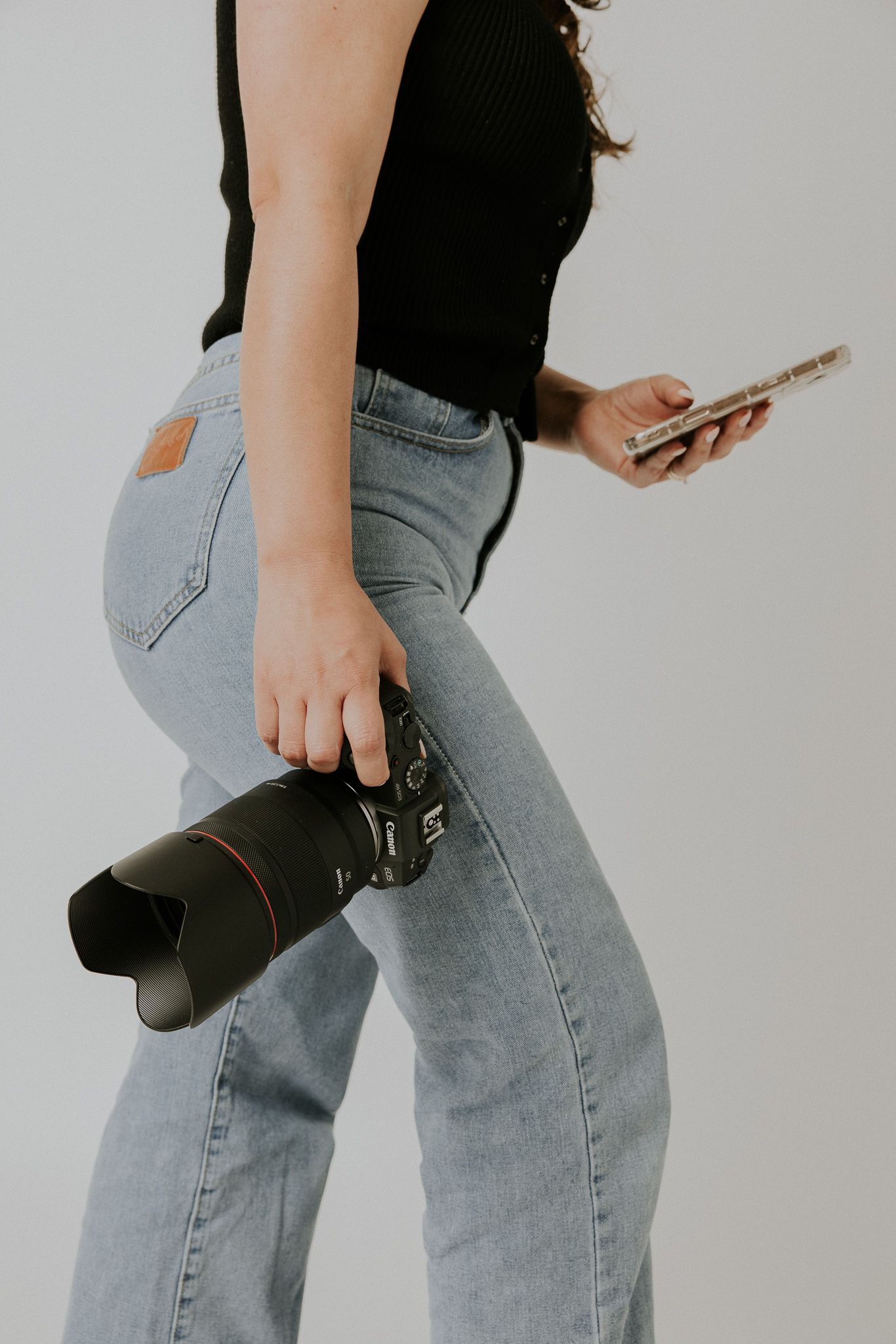 Person in jeans holds camera and phone displaying casual photography gear.