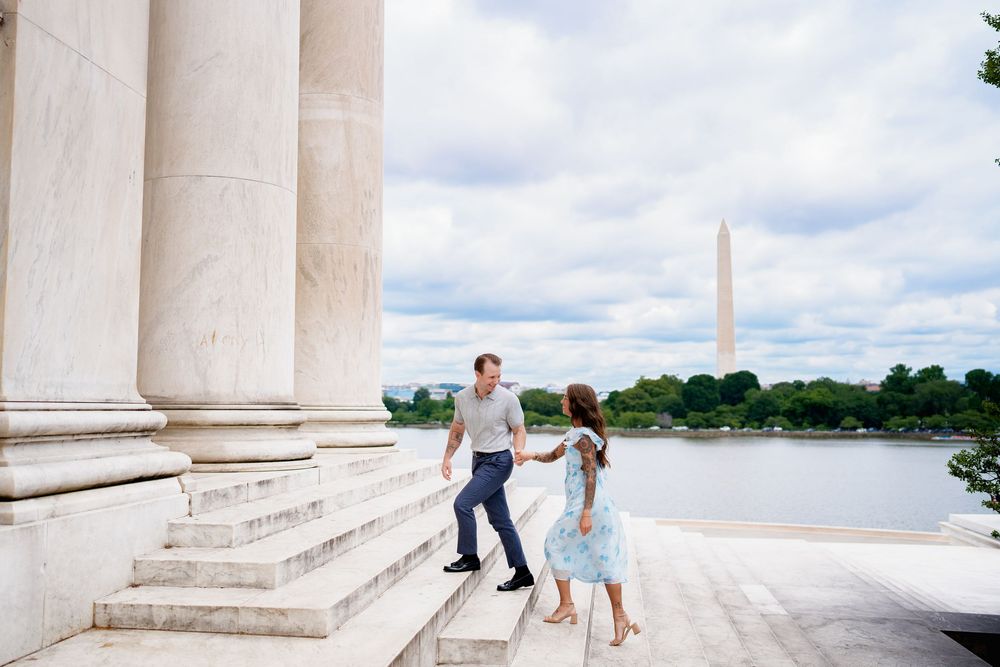 Couple holding hands on steps of Jefferson Memorial with Washington Monument and Tidal Basin in background, in Washington DC