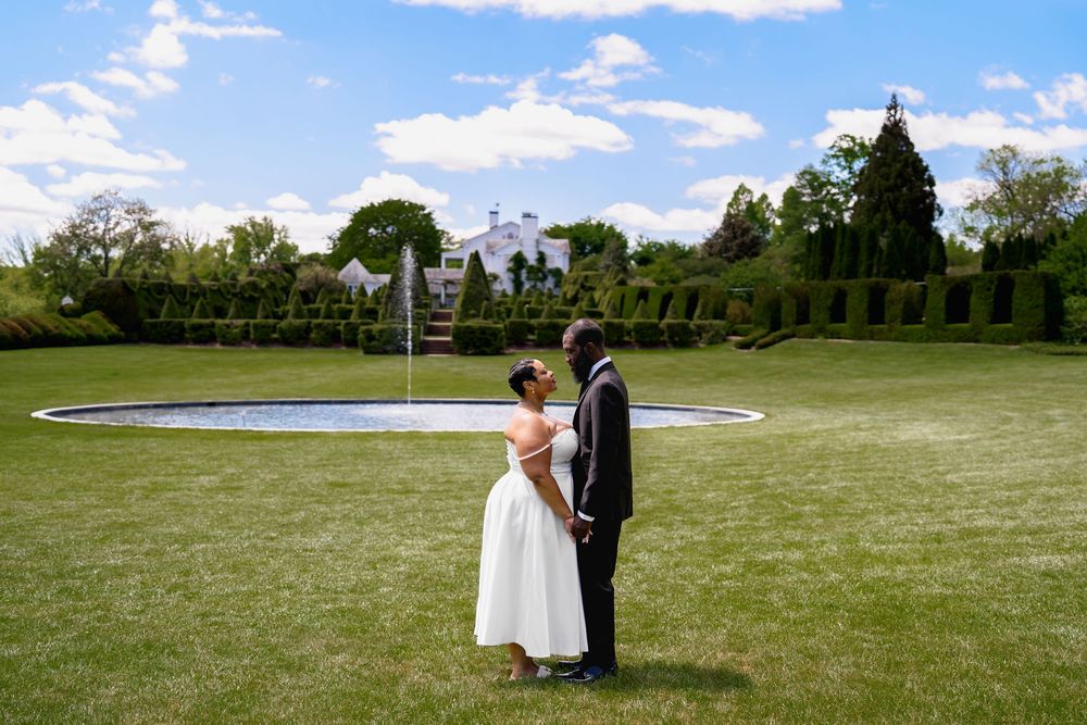 Bride and groom share a romantic moment on lush green lawn with elegant estate and manicured hedges backdrop, in Ladew Topiary Gardens, MD