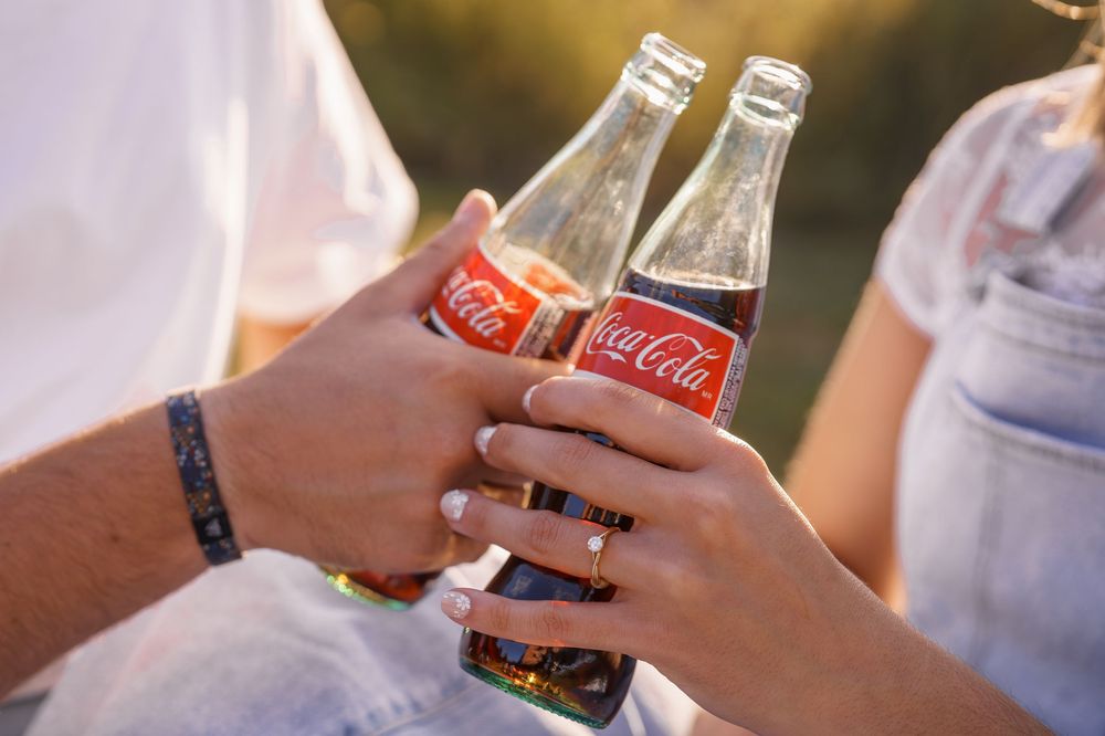 Close-up of hands holding glass beer bottles for a celebratory toast at an outdoor gathering, engagement in Frederick, MD