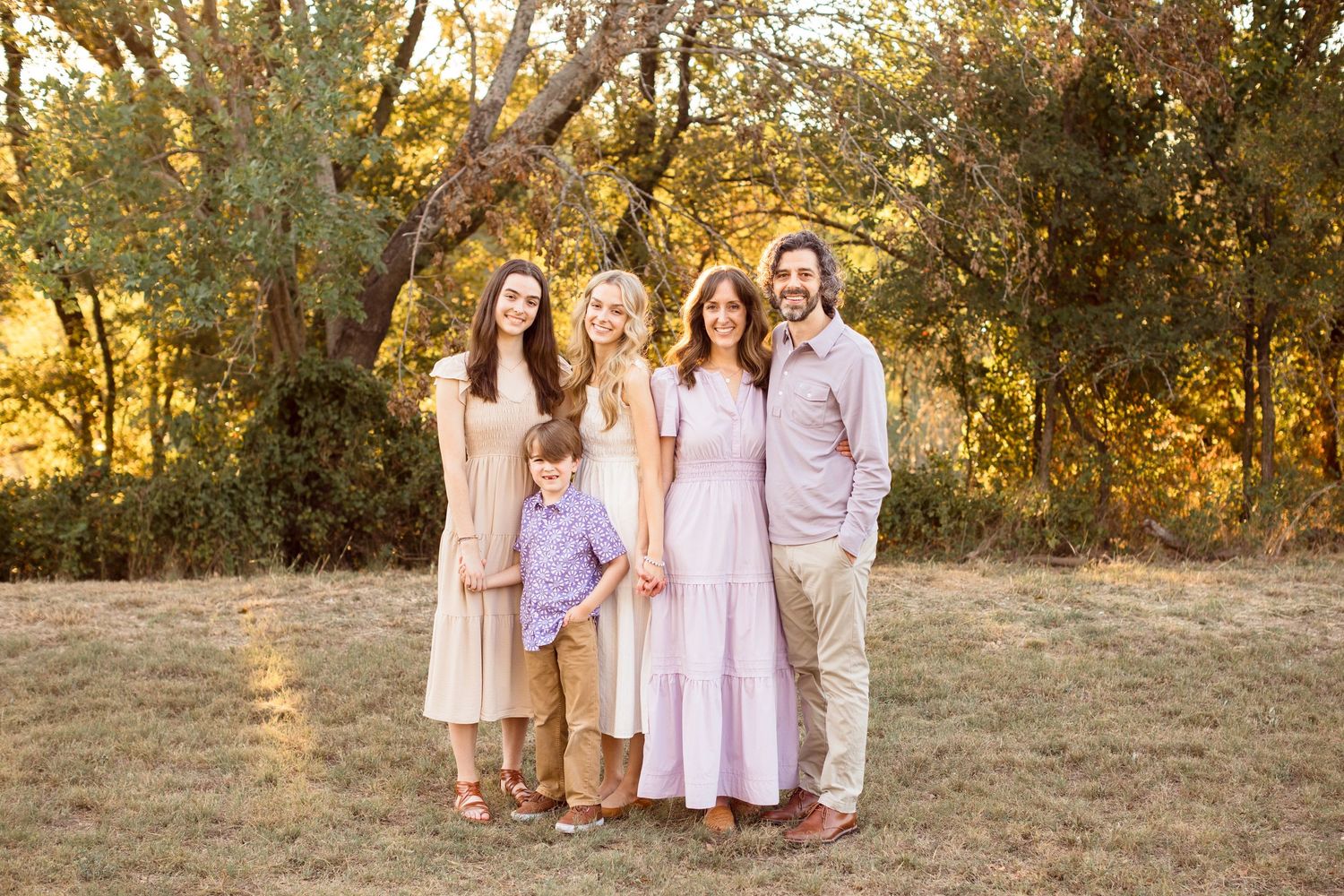 Family poses together at sunset wearing coordinated light-colored outfits in a natural outdoor setting.