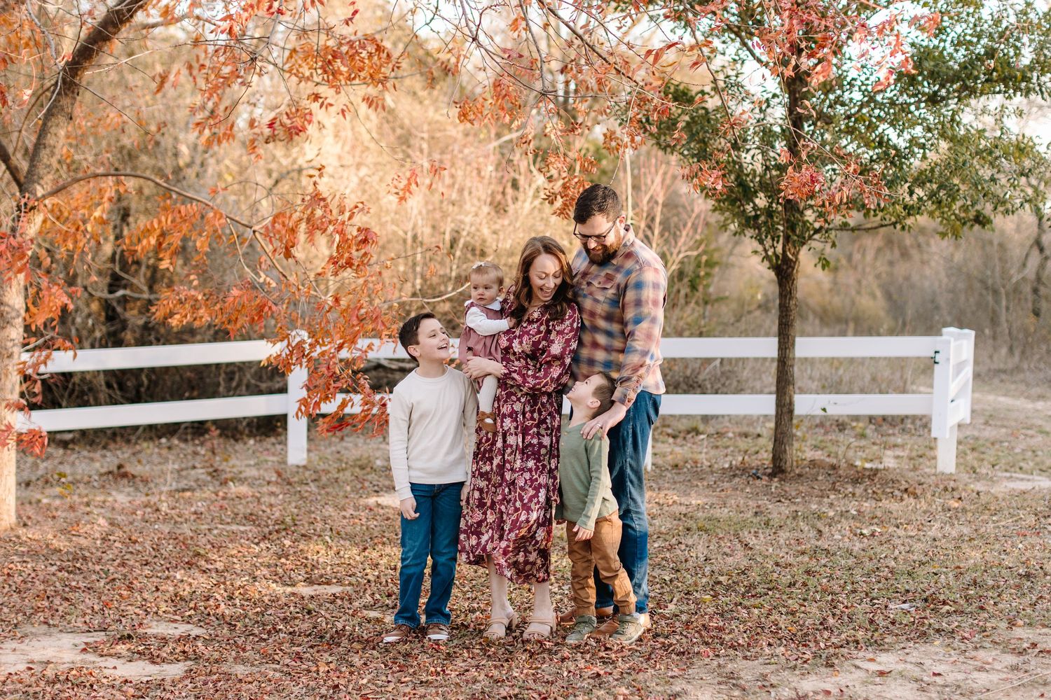 Family poses together at sunset wearing coordinated light-colored outfits in a natural outdoor setting.