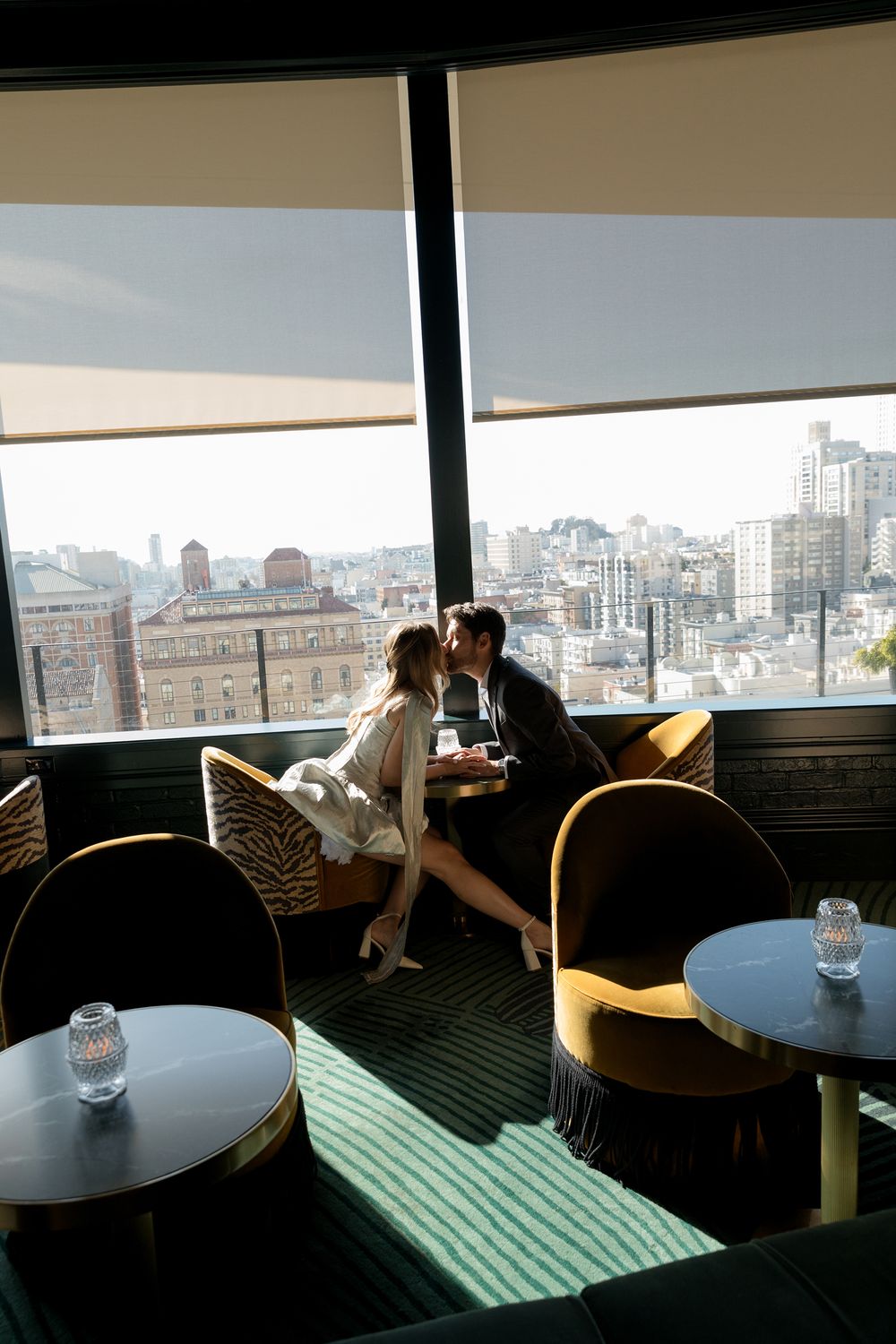 A panoramic view of a modern rooftop lounge with tables and seating against a city skyline backdrop.