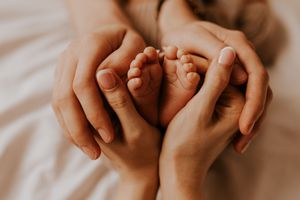 Gentle hands cradling small fingers in intimate close-up portrait.