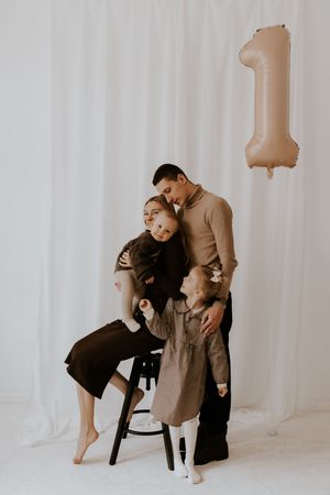 A heartwarming studio photoshoot with a small child and parent posing against a white backdrop with beige balloons.