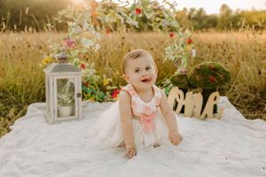 Sweet photoshoot setup in golden field with white lantern and decorative 'one' sign on blanket at sunset.