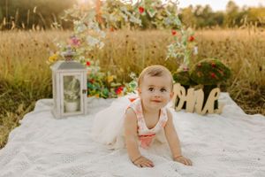Outdoor photo setup with white lantern and decorative letters on blanket in field at golden hour.