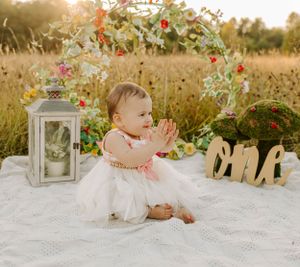Rustic outdoor photo setup with lantern and decorative elements on white blanket in field.
