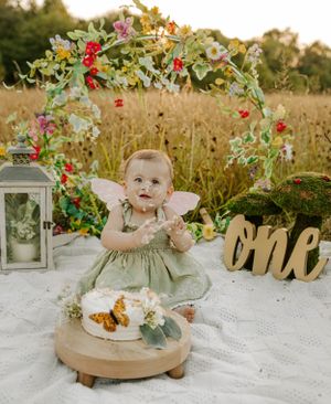 Delightful outdoor cake smash session with floral arch and vintage decorations in golden light.