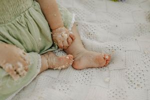 Close up of tiny feet and dress covered in cake crumbs on white lace blanket.