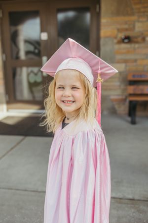 Graduate in pink cap and gown with tassel poses outdoors.