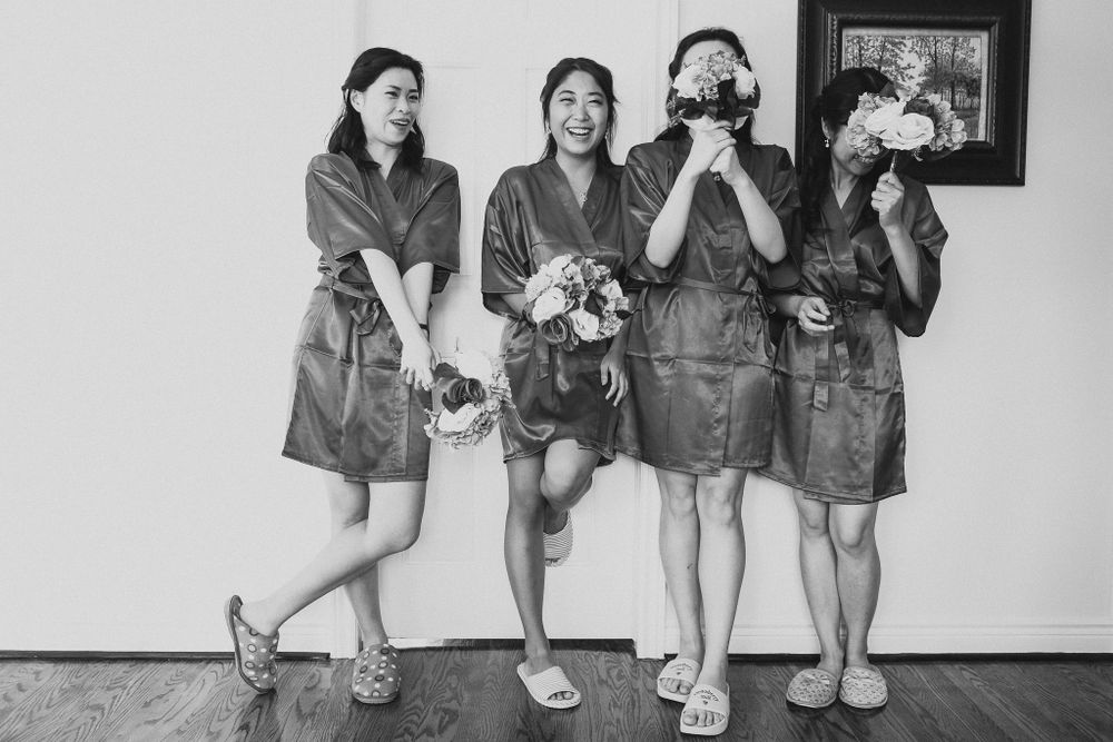 Four bridesmaids in matching dresses pose playfully covering their faces.