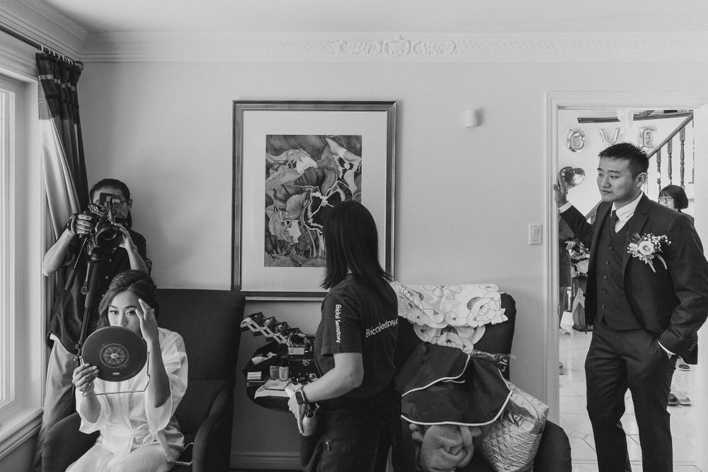 Candid black and white shot of wedding preparations in a room with artwork on the walls.