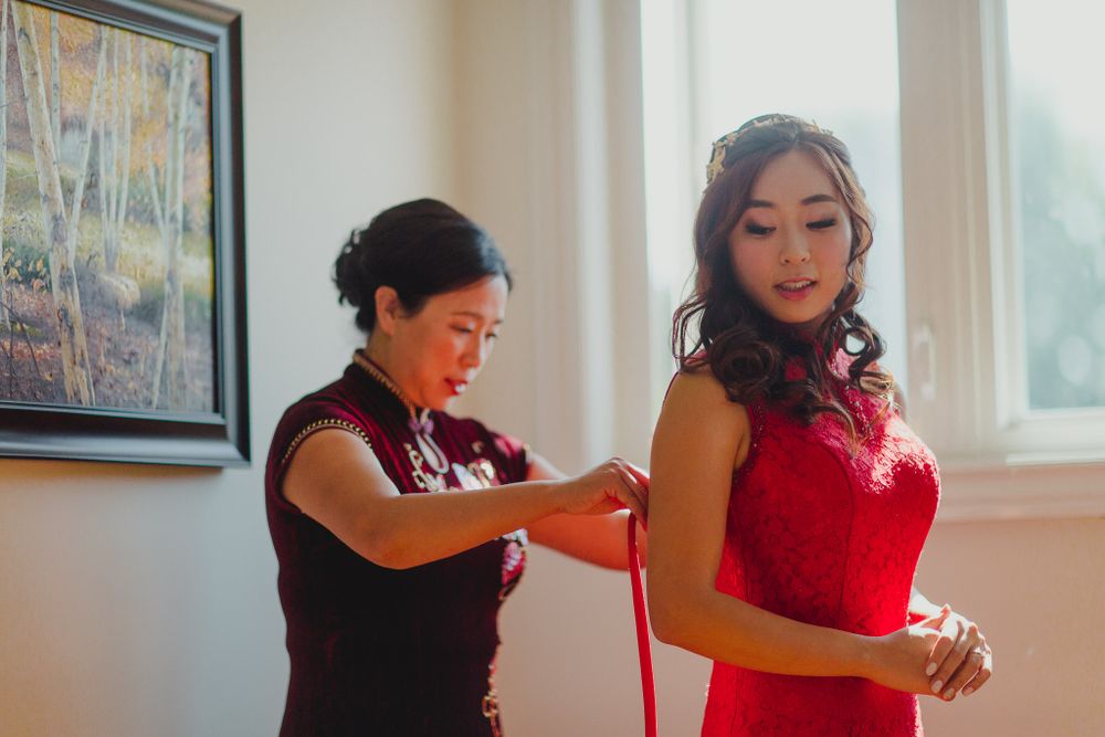 A woman in red dress getting final adjustments made to her outfit by a seamstress.