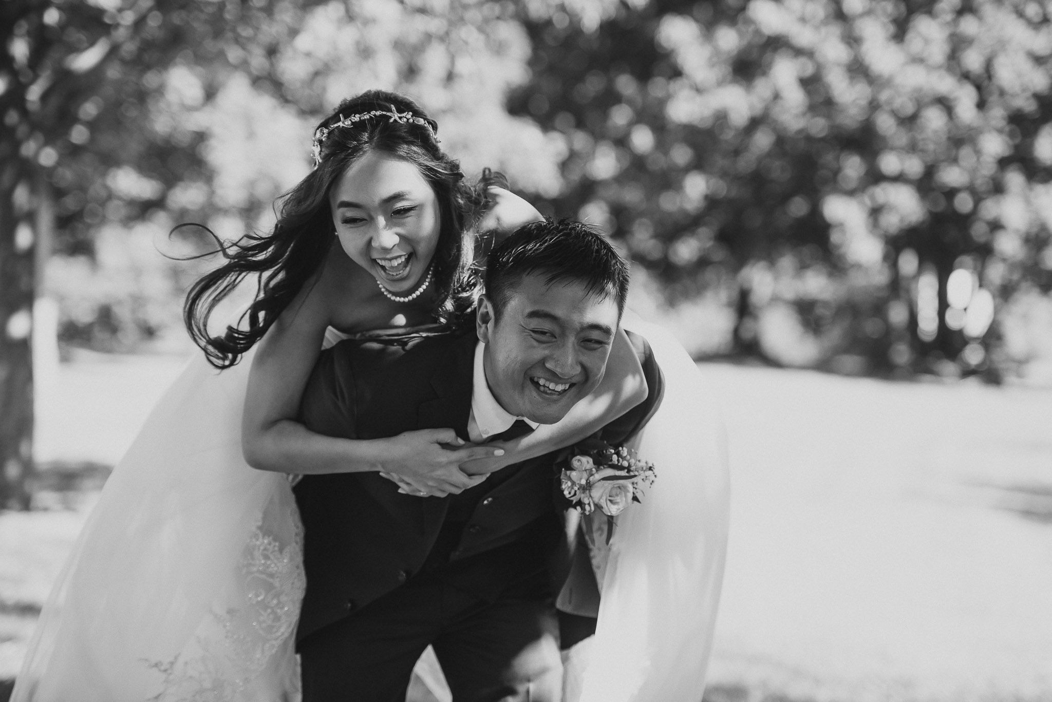 Joyful black and white photo of a piggyback ride in wedding attire.