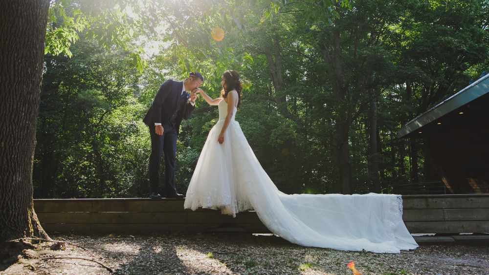 A couple in wedding attire share an intimate moment in a sunlit forest setting.
