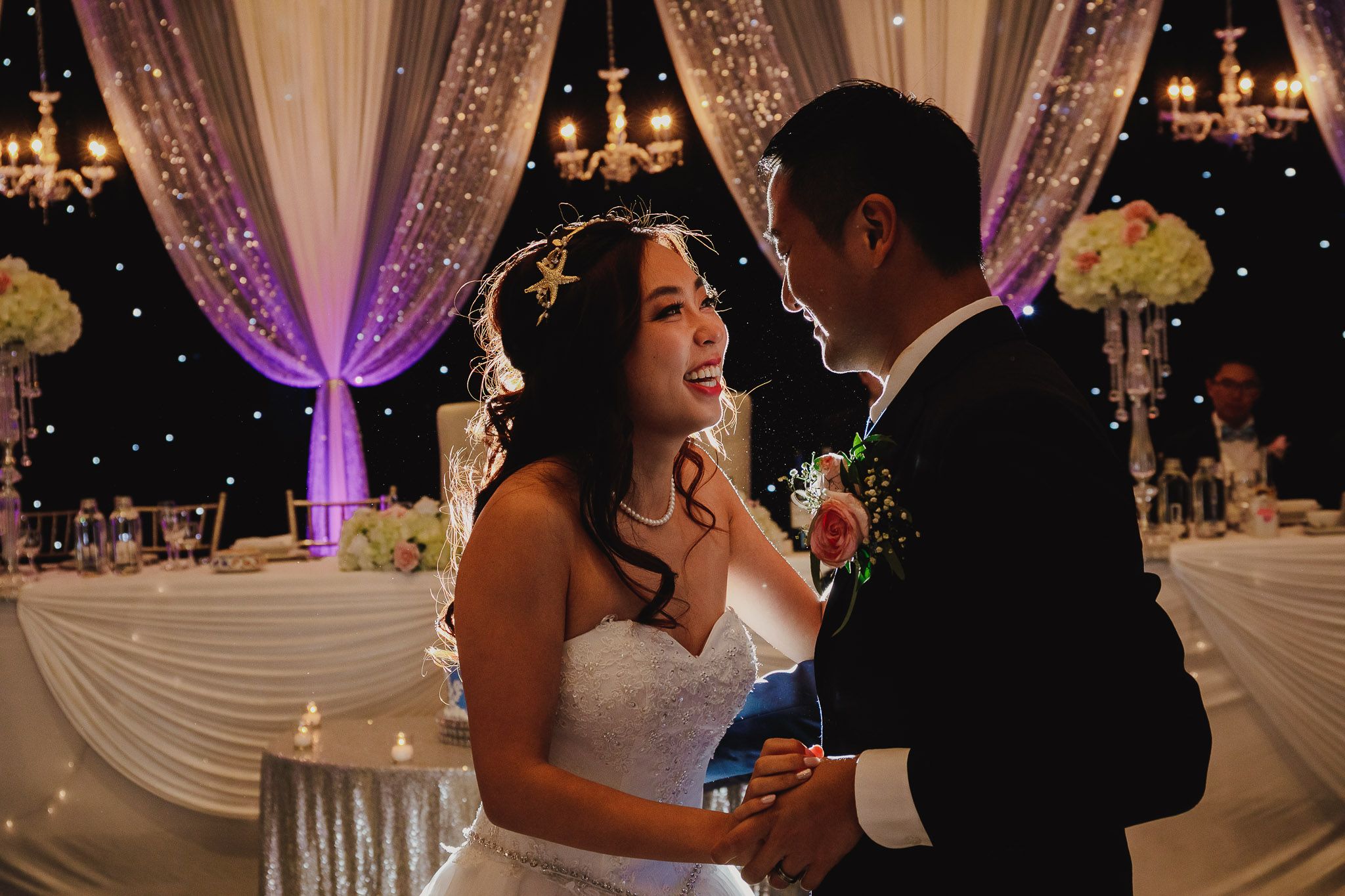 A couple shares an intimate moment on their wedding dance floor under purple lighting.