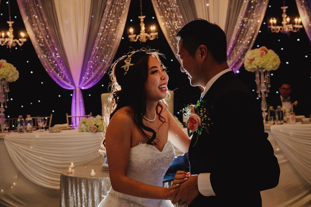 A couple shares an intimate moment on their wedding dance floor under purple lighting.