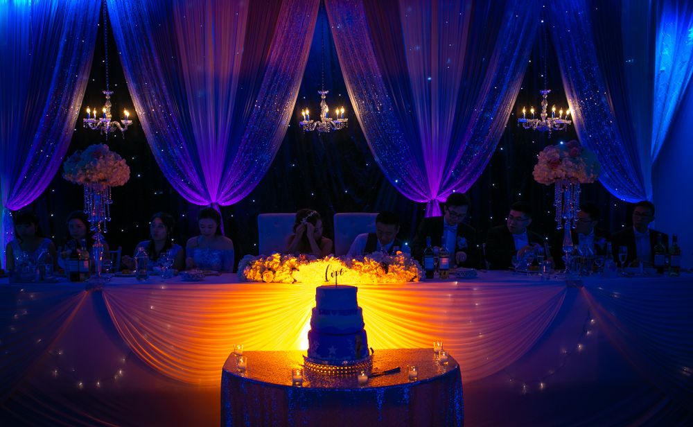 Elegant wedding reception setup with blue and purple uplighting highlighting a tiered cake display.