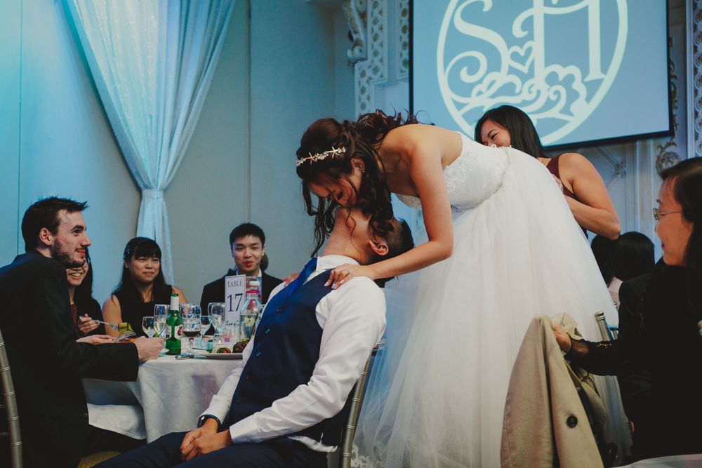 Playful wedding reception moment with couple at their dining table surrounded by guests.