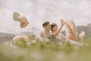 A couple shares a playful moment in a mountain meadow with distant peaks.