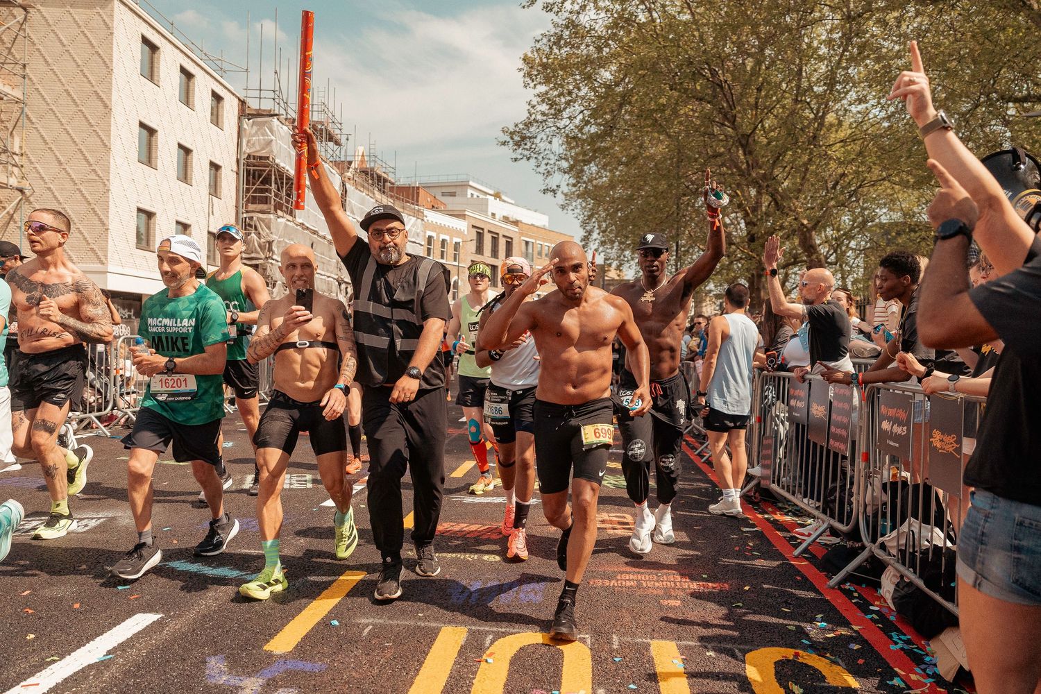 Energetic runners crossing finish line at marathon event while spectators cheer from behind barriers on city street.