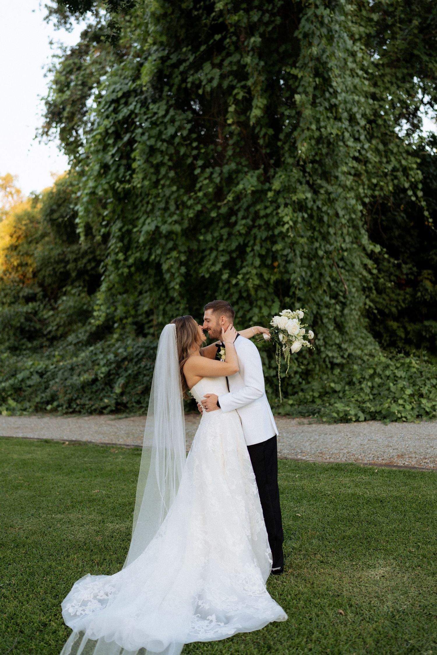 Bride and groom portraits, a romantic kiss outdoors, surrounded by lush green ivy-covered trees. Fresno California Wedding Photographer