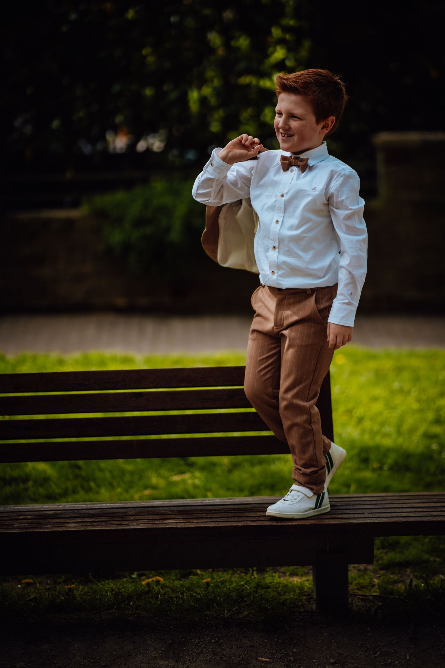 Stijlvolle pose op een houten bank in een park met formele kleding en vlinderdas.