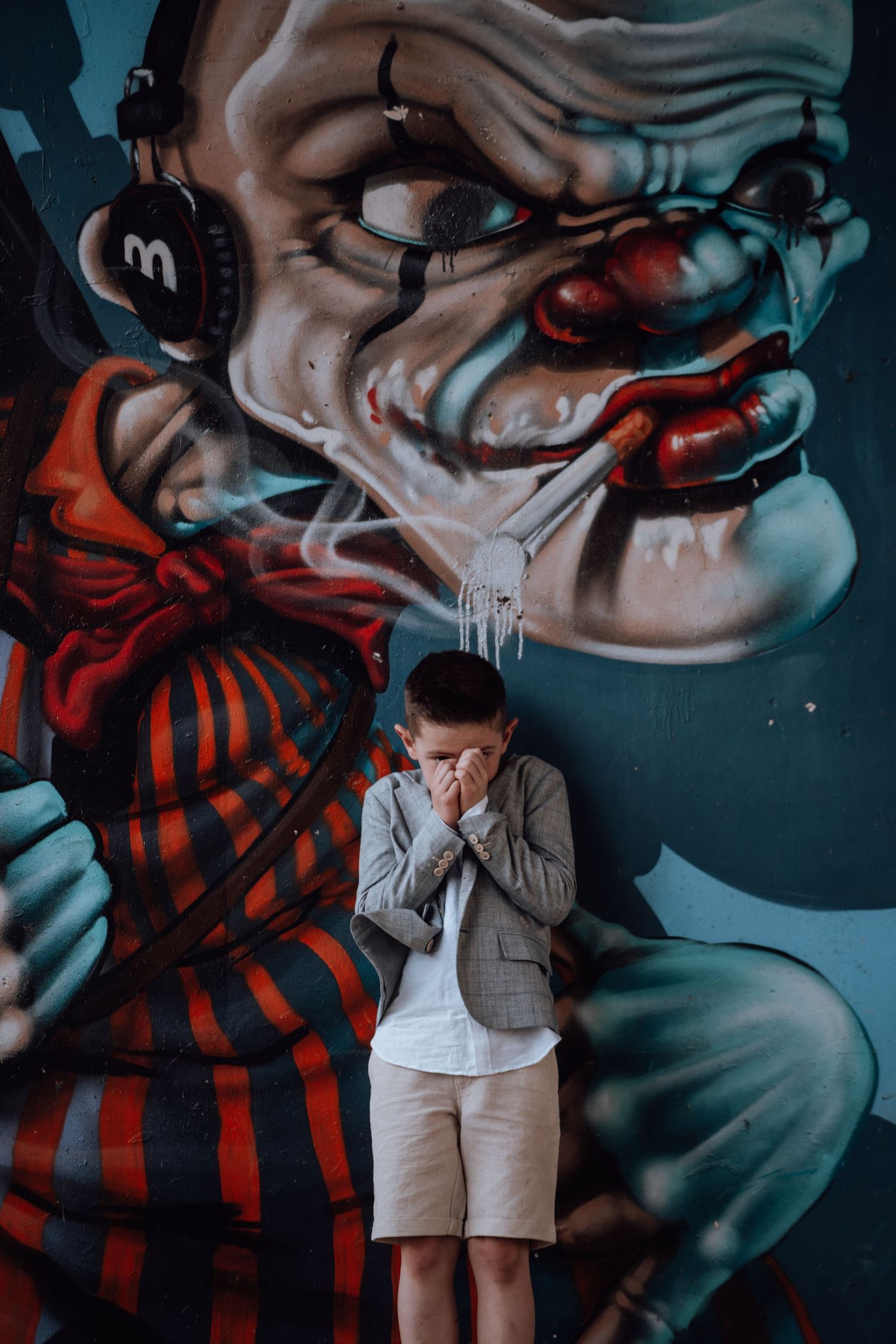 Dramatische pose tegen stedelijke straatkunst met een grote clownsmuurschildering met koptelefoon.