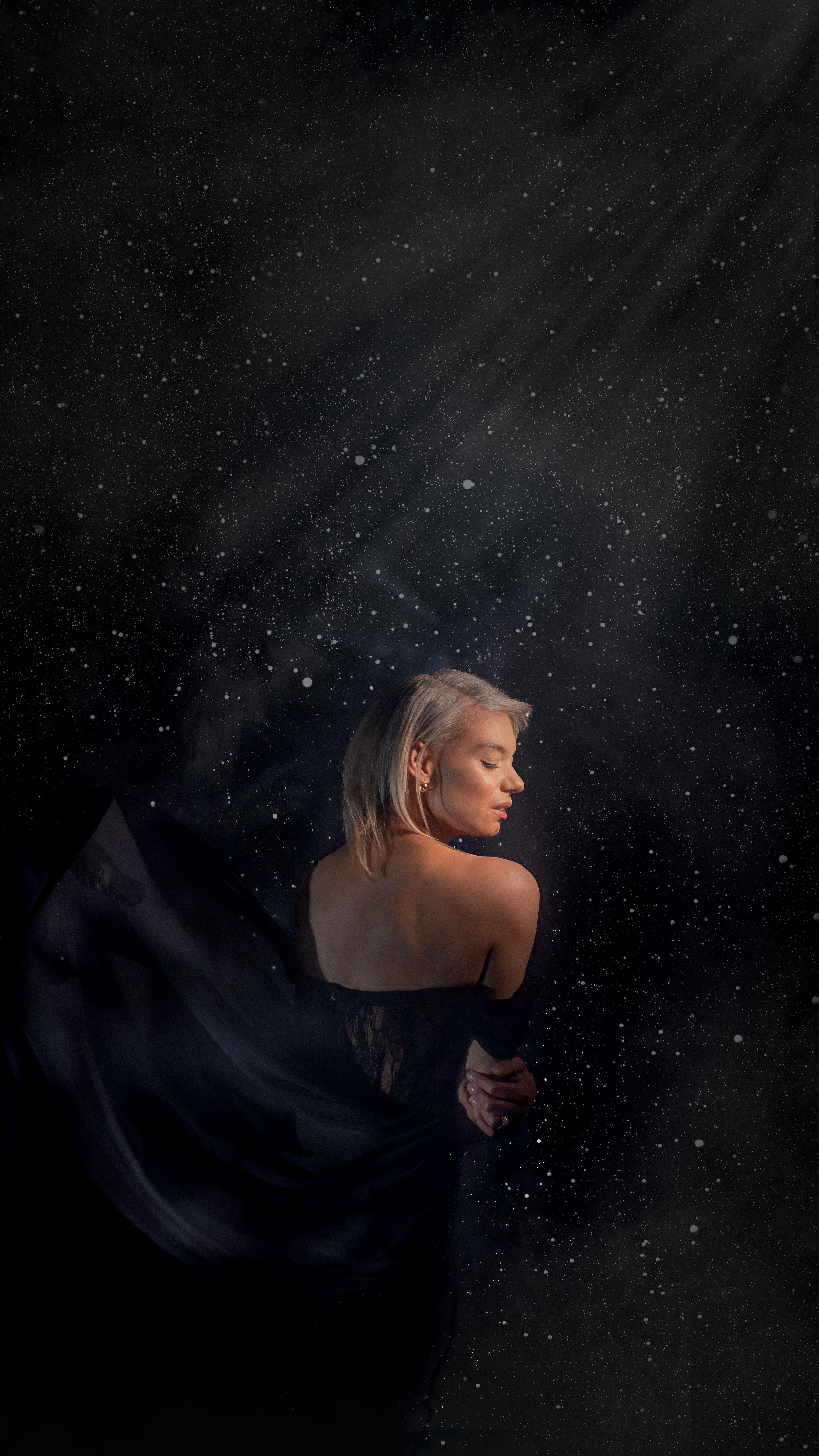 Artistic portrait against starry night sky with flowing dark fabric creating dramatic silhouette effect.