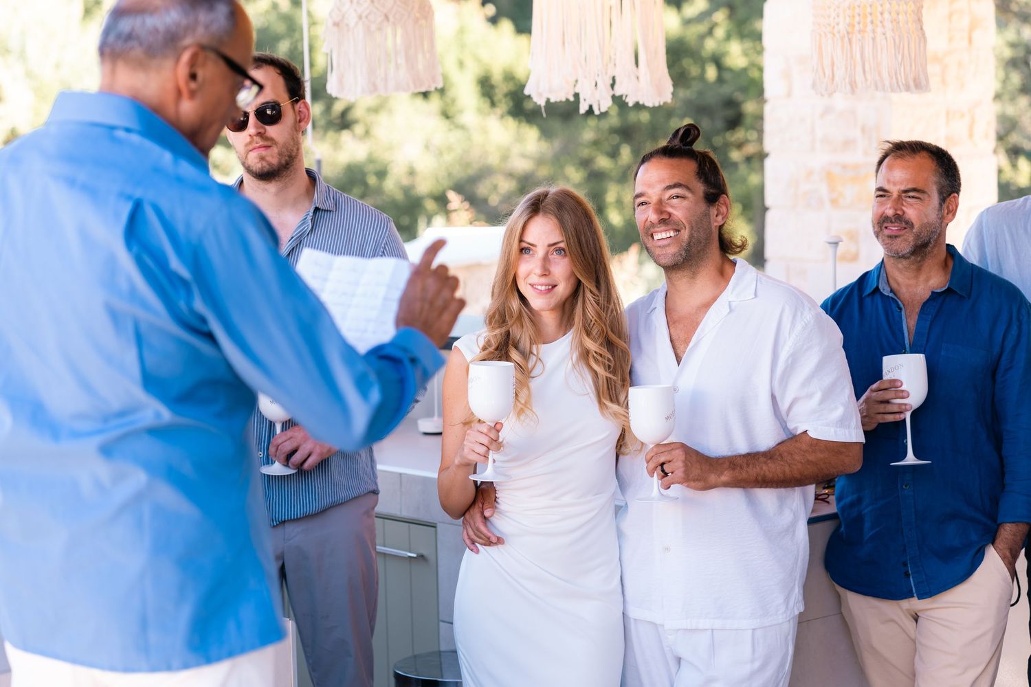 Guests in white outfits enjoying drinks and conversation at an outdoor gathering.