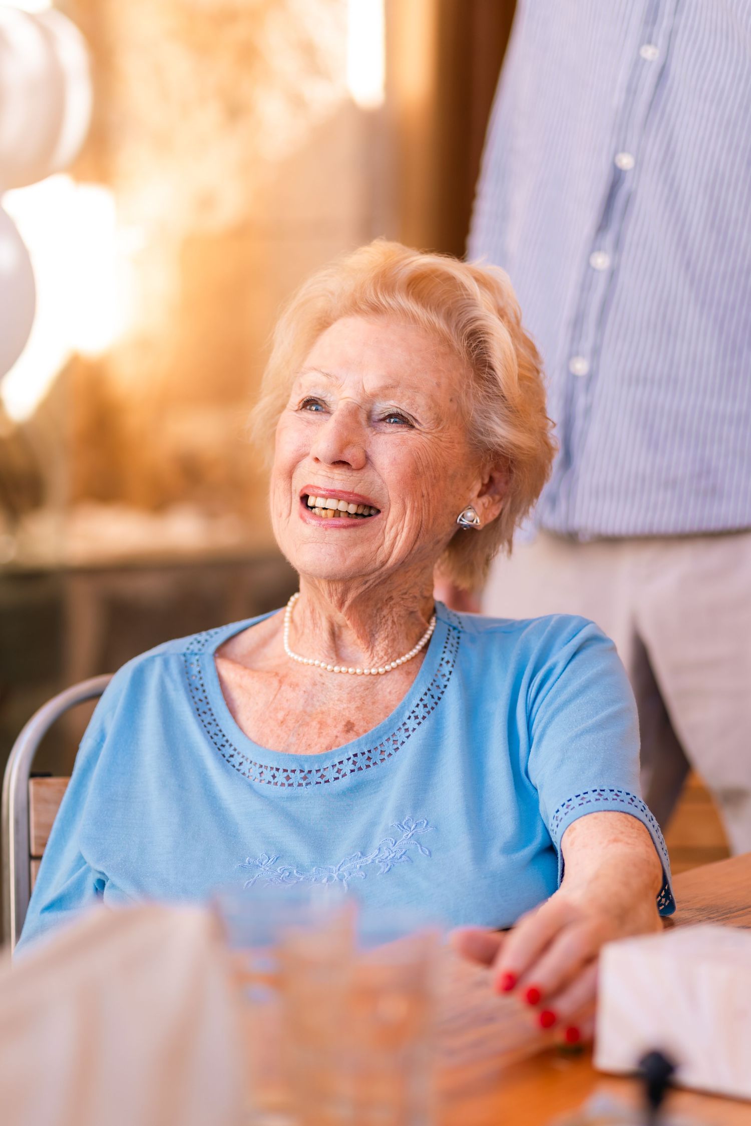 Person in light blue top smiling warmly while seated at table.