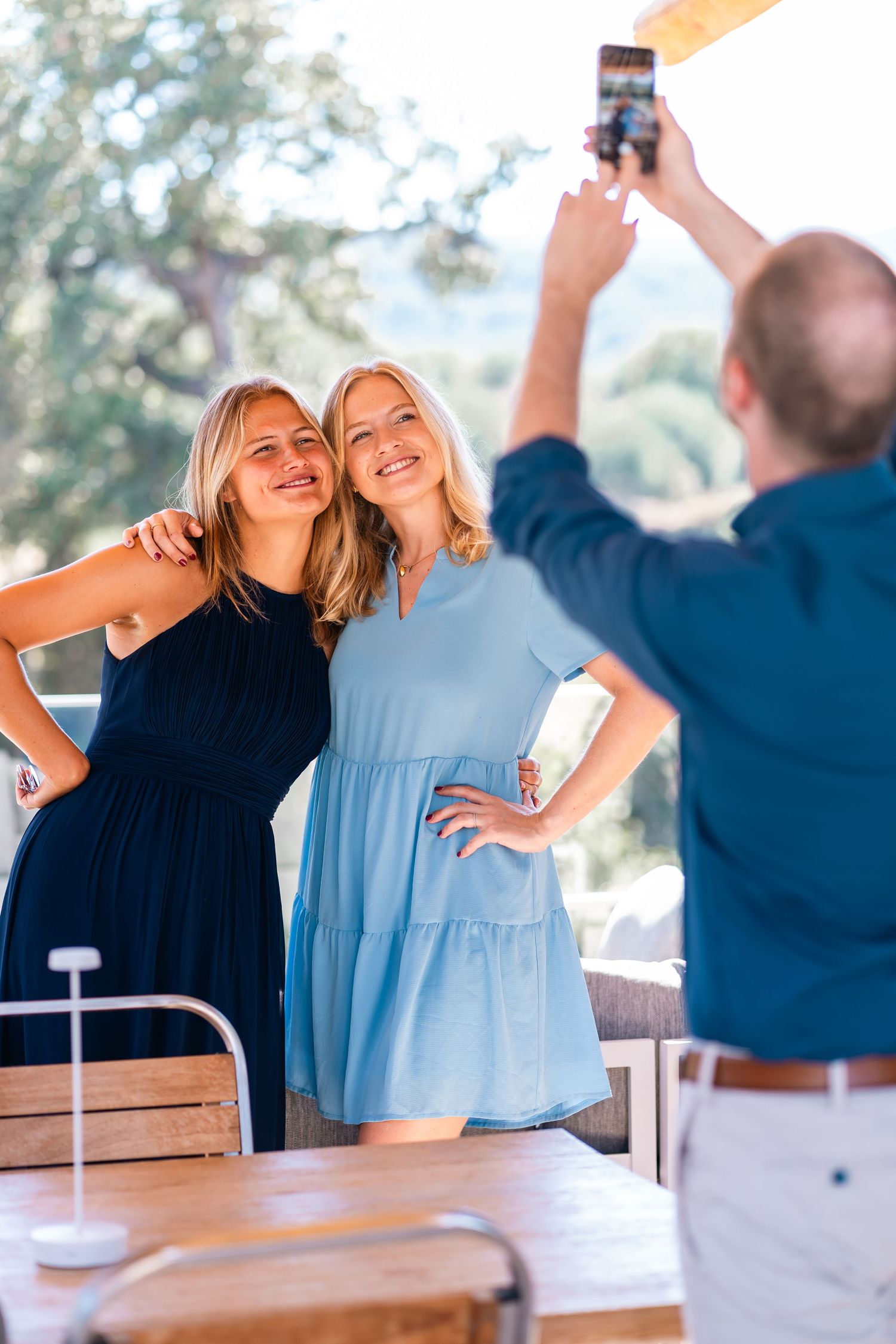 Two friends posing while someone takes their photo on outdoor patio.