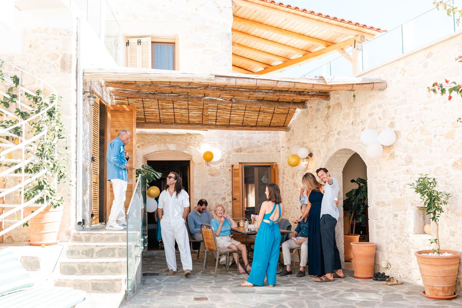 Guests gathered at a Mediterranean-style patio with stone walls and wooden pergola.