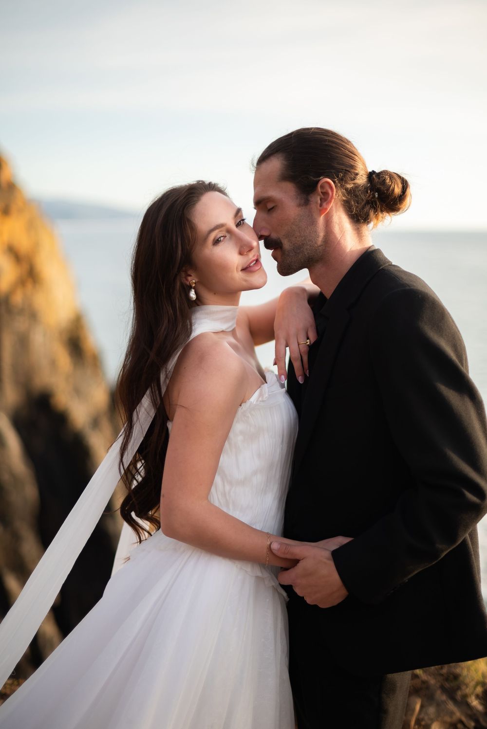A romantic coastal wedding photoshoot against dramatic cliffs at sunset.