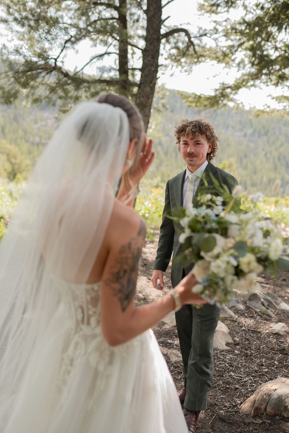 First look wedding moment captured on mountainside with flowing veil and white bouquet.
