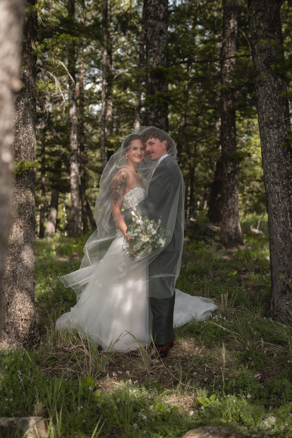 Intimate forest wedding moment with sunlight filtering through pine trees.