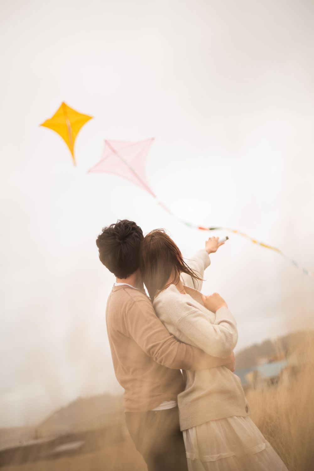 A dreamy engagement photo with flying kites in a misty field.