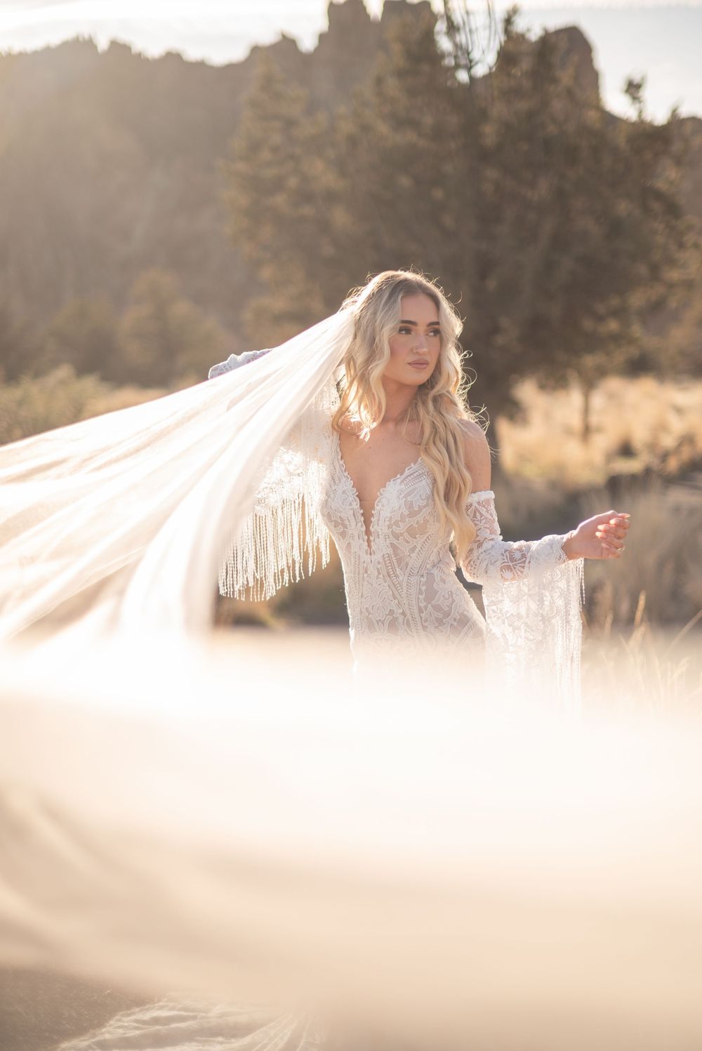 Ethereal bridal portrait with flowing veil and soft golden sunlight in a dreamy outdoor setting.