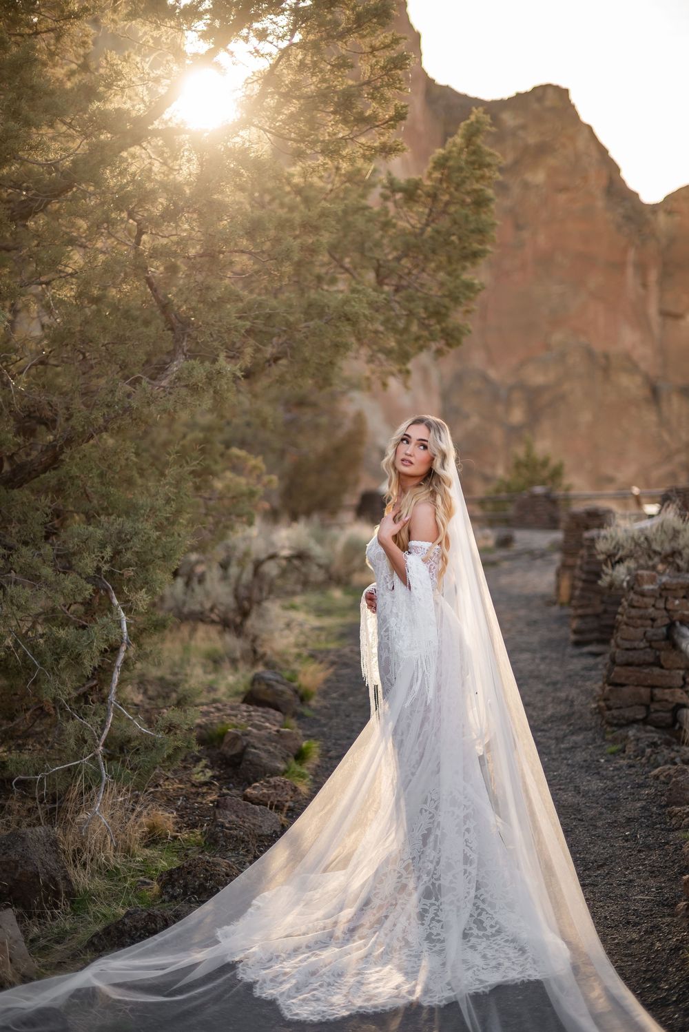 A flowing white wedding dress catches golden sunlight against a rocky desert backdrop.