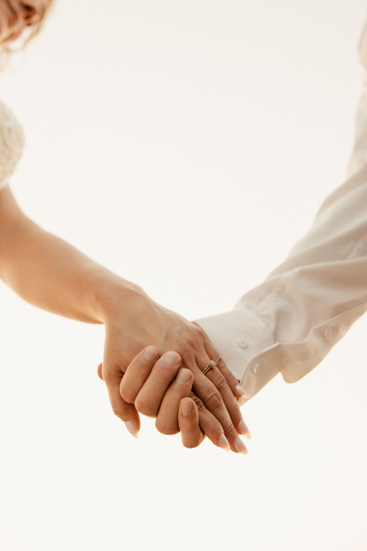Close-up of hands tenderly clasped together against white background.