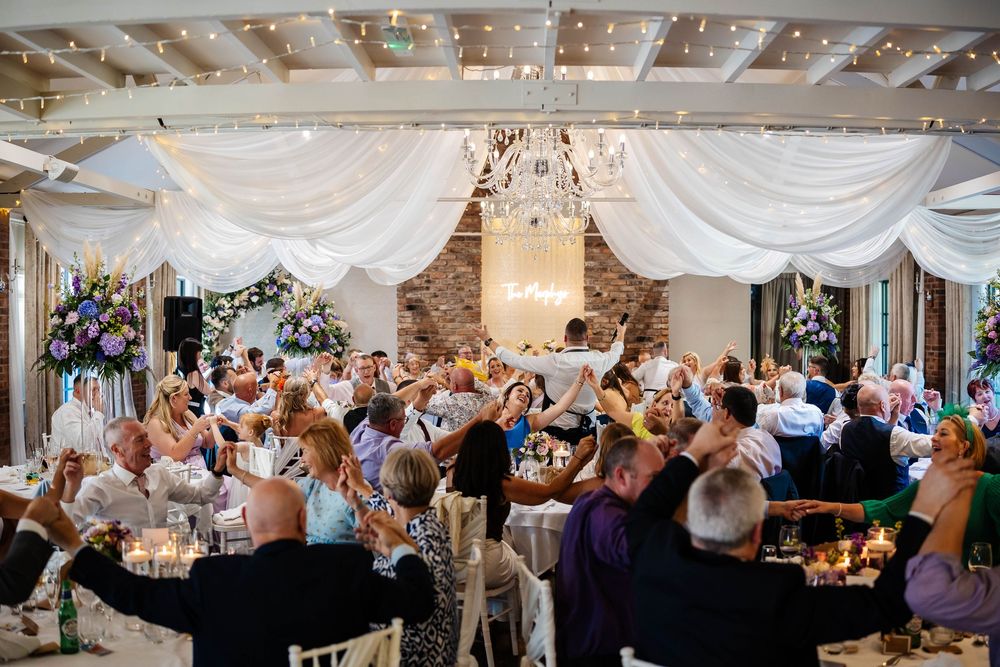 Wedding guests wave white napkins in celebration during wedding breakfast, hosted by The Undercover Waiters Ltd at Bartle Hall Wedding