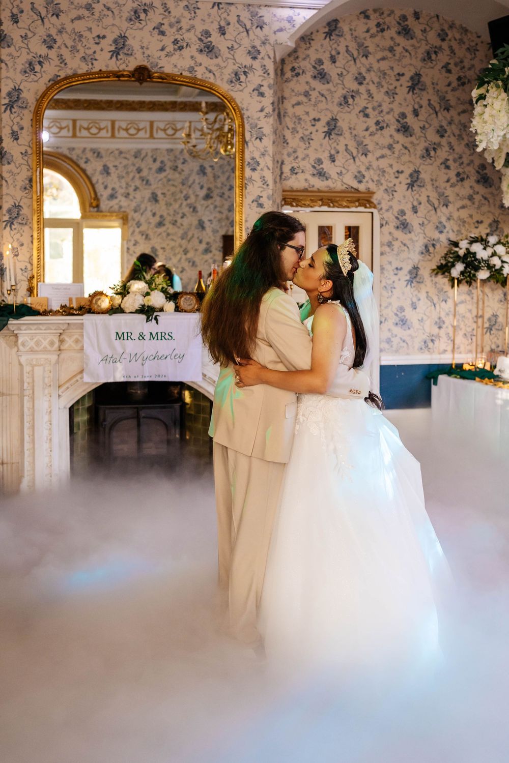 Bride & Groom share a first dance kiss surrounded by dry ice in an elegant floral wallpapered venue with a Mr. & Mrs. sign at Rushpool Hall