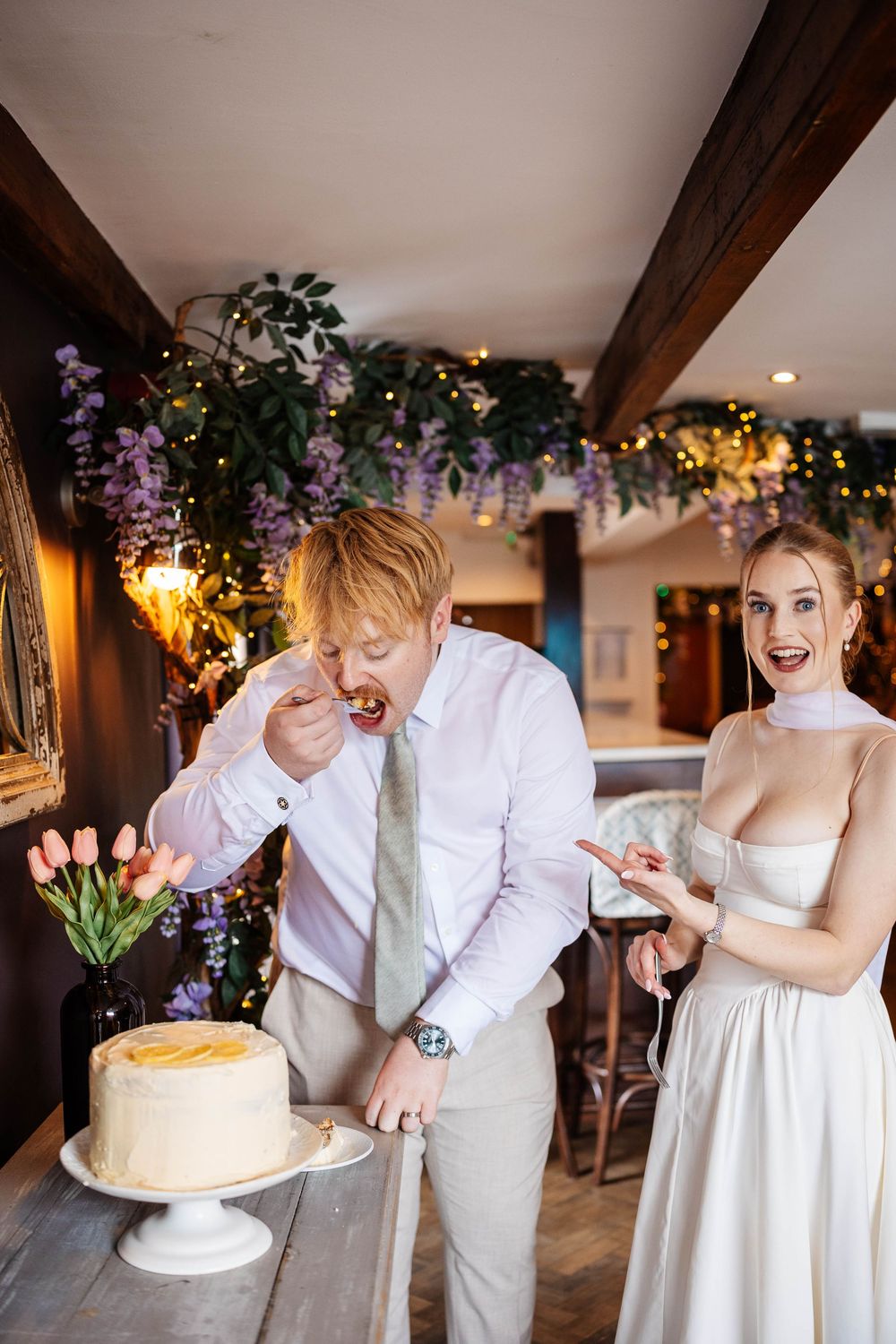 A couple in white sharing their first slice together at their reception captured at Botanic Road Eatery, Churchtown, Southport