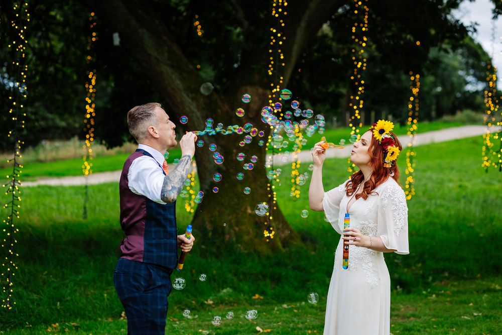 bride & groom blowing bubbles at their Tipis at Riley Green wedding, surrounded by fairy lights captured by Lynette Matthews Photography