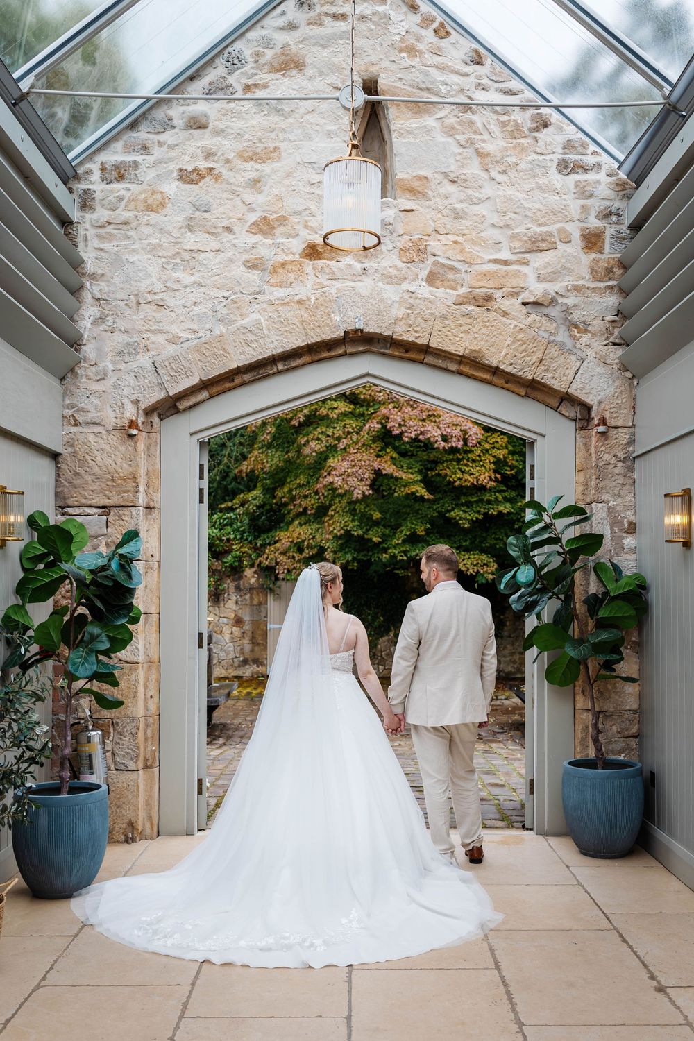 Bride and groom holding hands walking through stone arch doorway in an elegant venue at Wyresdale Weddings by Lynette Matthews Photography